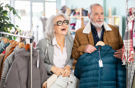 Mature married couple chooses fashionable down jacket or coat in clothing storeの写真素材