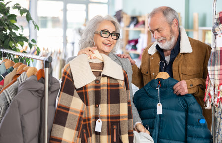 Mature married couple chooses fashionable down jacket or coat in clothing storeの写真素材