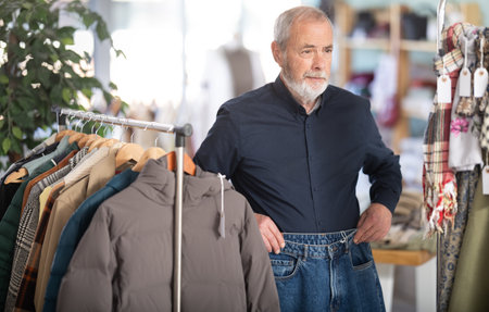 Elderly male shopper chooses fashionable jeans in clothing storeの写真素材