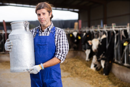 Male farm worker carrying big milk can walking in cowshed on dairy farmの写真素材