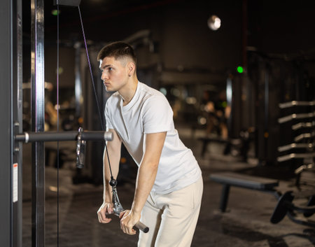 In gym, man uses cable row machine to strengthen muscles.