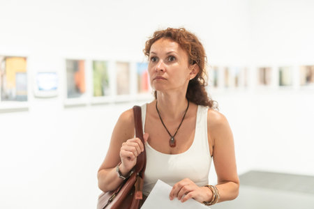 Middle-aged woman looking at pictures on wall in museumの写真素材