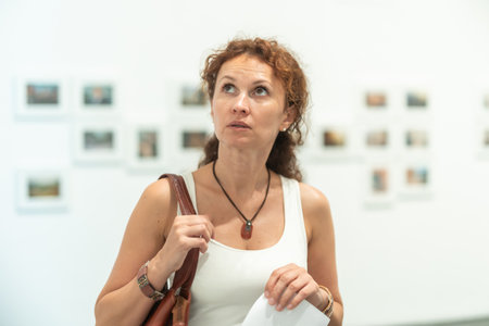 Middle-aged woman looking at pictures on wall in museumの写真素材