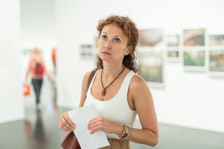 Middle-aged woman looking at pictures on wall in museumの写真素材