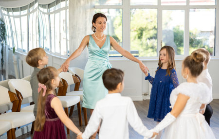 Little children in elegant dresses doing round dance in a hall