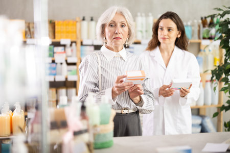 Elderly woman choosing packages of pills and medicines with pharmacist at pharmacyの写真素材