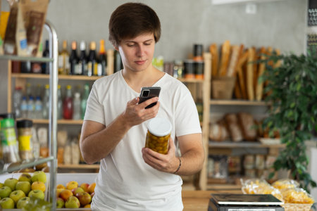 Young man scans a jar of olives on his phoneの写真素材