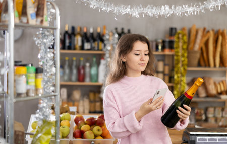 Female buyer purchaser scanning with smartphone QR code label of bottle of wine in shopの写真素材