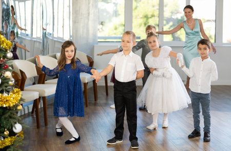 Little children standing in pairs in school-hall decorated with Xmas treeの写真素材
