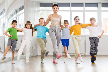 Smiling preteen children learning to dancing folk dance in row in studio