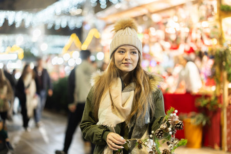 Girl with cone and fir brunch garland stands in middle fair decorated for New Year holidaysの写真素材