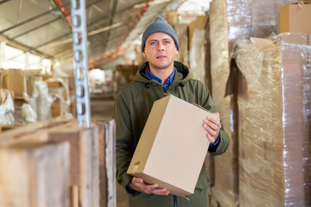 Worker holding cardboard box while standing in storehouse