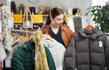Adult woman chooses down jacket in clothing storeの写真素材