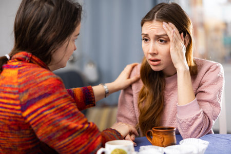 Sad woman sitting at table with her friend who supporting her