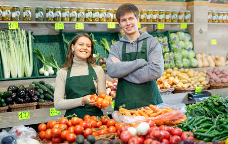 Young male and female sellers posing in grocery market with tomatoes in hand