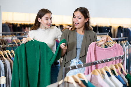 Portrait of two positive women choosing cardigan in clothing shopの写真素材