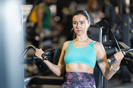 Athletic woman using biceps curl machine during training in gym