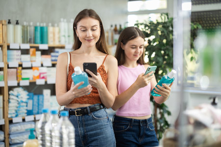 Mother and daughter in summer clothes scans code on medicinal mouthwash to check expiration dateの写真素材