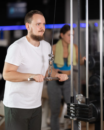 Man in gym performs exercises for arm muscles using cable crossover machine and pull weighted rope