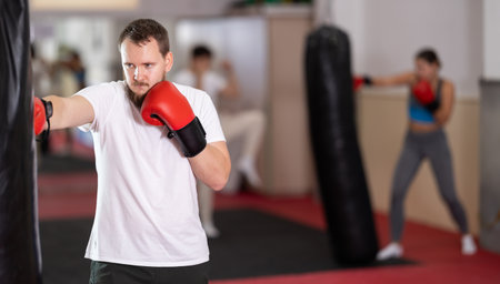 Bearded man punches and kicks punching bag in gym.の写真素材