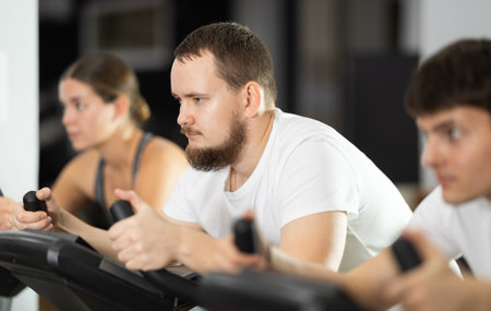 Focused bearded man works out with stationary bicycle during class at fitness club