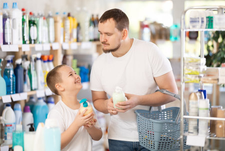 Schoolboy son and dad are choosing liquid hand soap in storeの写真素材