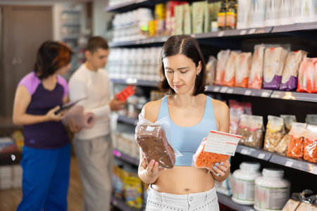Middle-aged woman choosing whole-grain pasta or bread in sports nutrition storeの写真素材