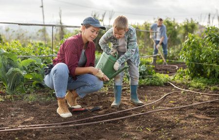 Woman planting seeds boy watering beds
