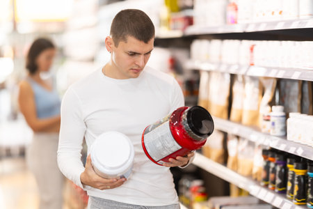 Young guy choosing protein powder jar in sports nutrition storeの写真素材