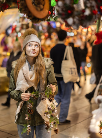 Girl with cone and fir brunch garland stands in middle fair decorated for New Year holidaysの写真素材