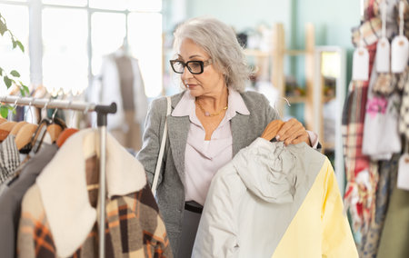 elderly woman chooses a down jacket in storeの写真素材