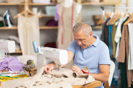 Man tailor sews on sewing machine in workshop