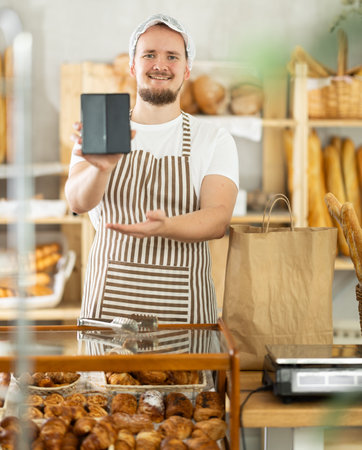 Guy seller in bakery hold out hand with phone, points at screen with finger