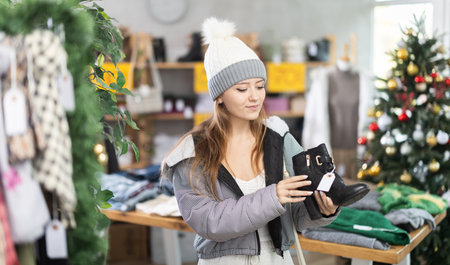 Girl client looks at products in store, looks closely at heeled ankle boots, picks up wardrobe itemの写真素材