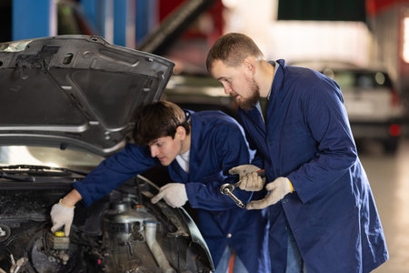 Two auto mechanics work together to diagnose an engine under the hood of a car in repair shop