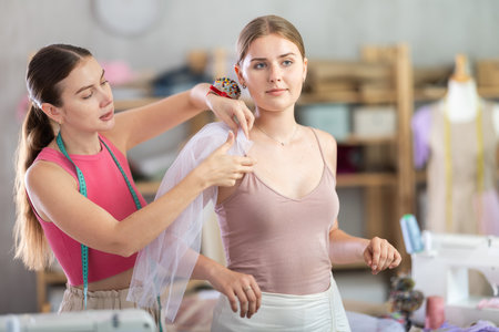 Adult female seamstress adjusting clothes on young womanの写真素材