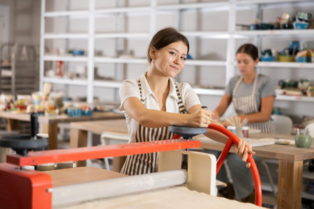 Girl student in pottery workshop works with machine clay press roller