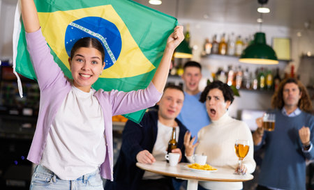 Emotional young adult fans supporting sports team with state flag while resting with beer in barの写真素材
