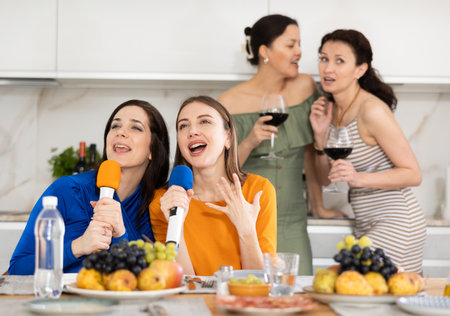 Cheerful slightly tipsy women singing with microphones at home karaokeの写真素材