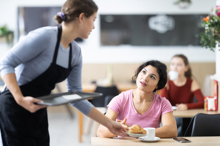 Polite waitress brings coffee and croissant to young girls in cafeteriaの写真素材
