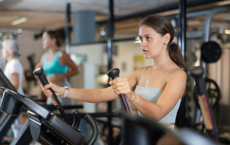 Slender athletic girl during cardio exercises on elliptical simulator in fitness center.の写真素材