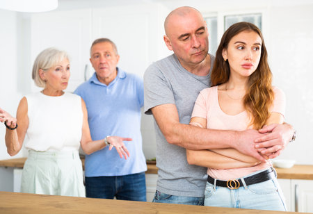 Husband and wife listen to their parents scold them in home kitchenの写真素材