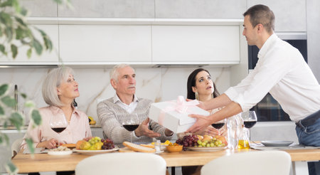 Caring son-in-law surprising father-in-law with present during family feastの写真素材