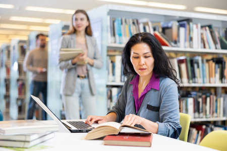 Asian woman working with laptop and books on science project in library