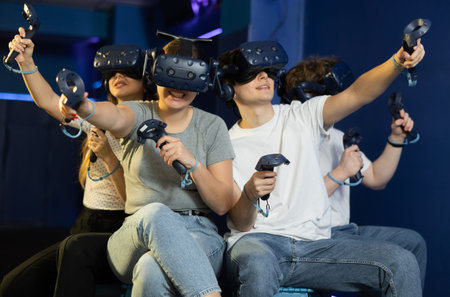 group of four friends wearing virtual reality glasses and with joysticks sit and play dynamic game