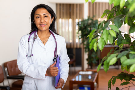 Smiling female doctor with clipboard standing in waiting room of clinicの写真素材