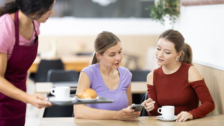 Girl waiter in apron presents coffee and croissants to restaurants guests.の写真素材