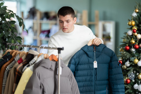 Male shopper choose down jacket in clothing store before Christmas