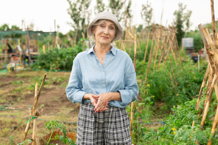 Happy elderly woman posing in her garden, in the backyard of village houseの写真素材