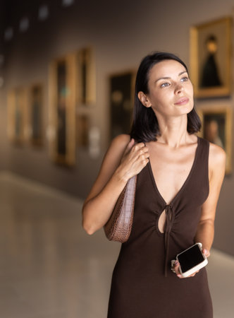 Woman visiting museum and looking at paintings in gold framesの写真素材